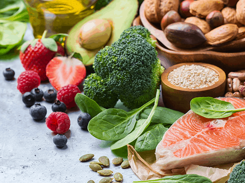 Healthy foods including salmon, spinach, broccoli, berries, and nuts arranged on a table.