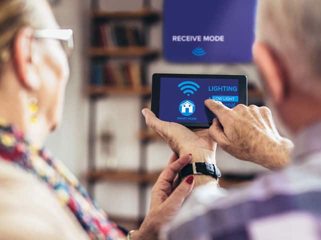Elderly couple using a tablet to control smart home lighting in their unit.