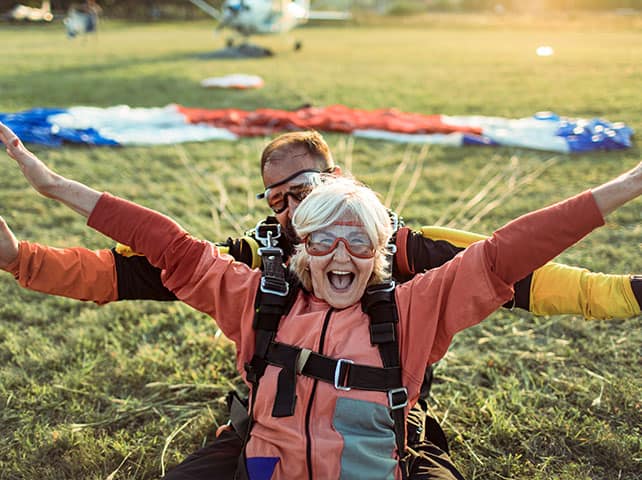 Senior woman enjoying tandem skydiving with an instructor in an open field.