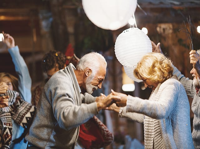 Senior residents joyfully dance at a communal gathering with paper lanterns overhead.