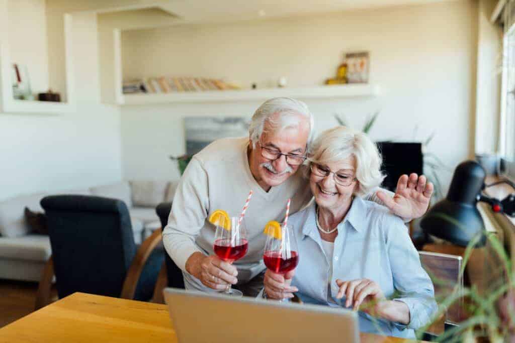 Senior couple enjoying drinks and using a laptop in a living space.