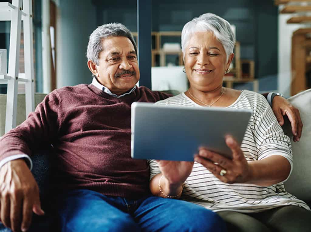 Smiling senior couple seated on a couch using a tablet together.