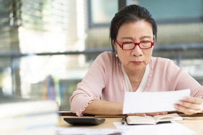 Older woman with red glasses reviewing finances at a desk in a bright room.