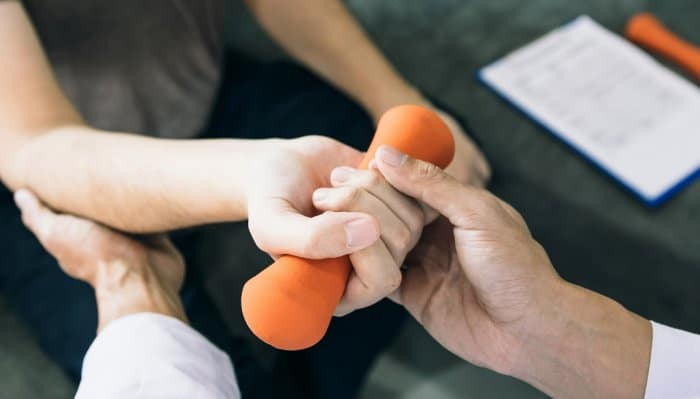 A physical therapist assisting a resident with an orange dumbbell exercise.