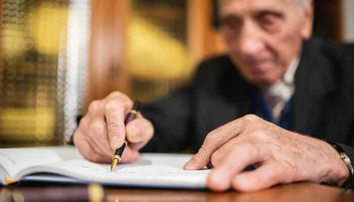 Elderly man in suit signing documents at a desk in a senior living community