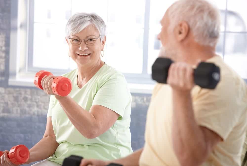 Senior individuals exercising with dumbbells in a well-lit fitness area.