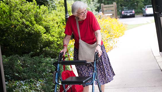 Elderly woman using a walker on the sidewalk in a senior living community.
