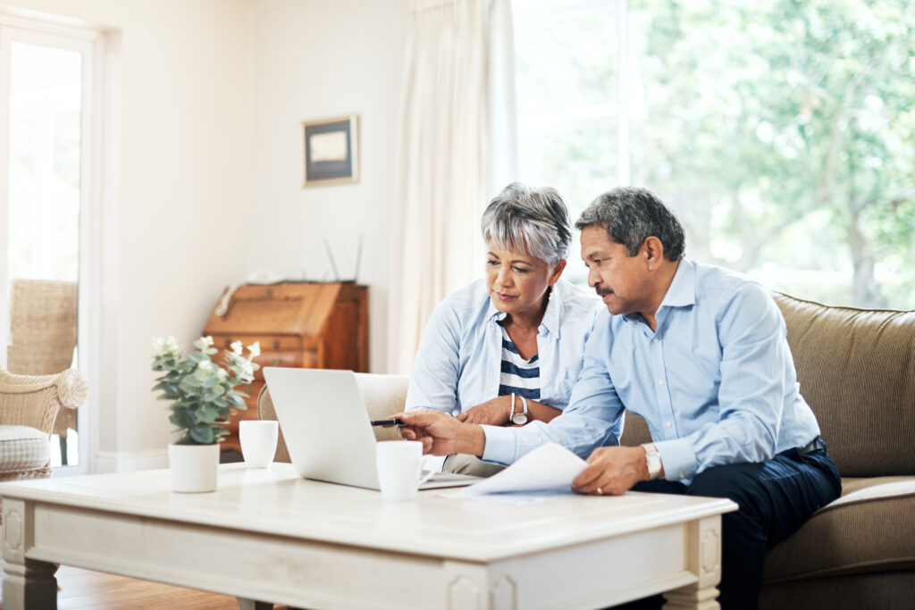 Senior couple reviewing financial documents on a laptop at home.