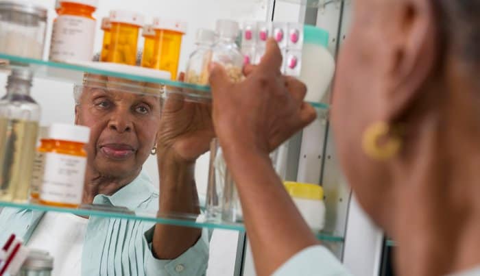Senior woman organizing medications in her bathroom medicine cabinet in her unit.