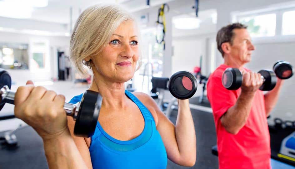 Senior woman and man lifting dumbbells in a fitness center, focused on their workout.