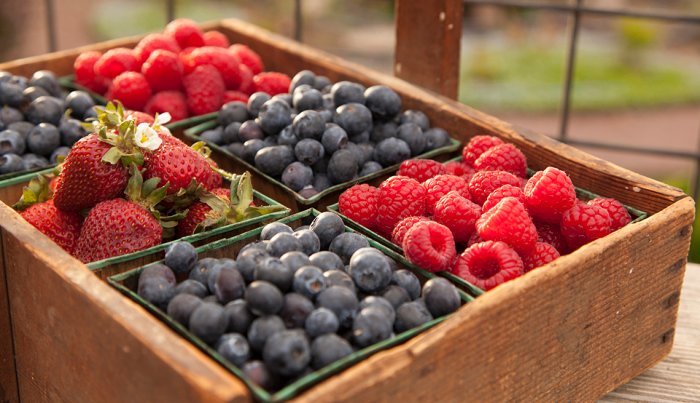 Close-up of various fresh berries, including strawberries, blueberries, and raspberries, in a wooden tray.