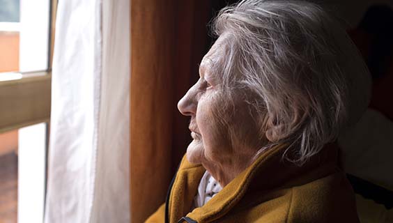 Older adult with white hair looking out the window with a thoughtful expression.