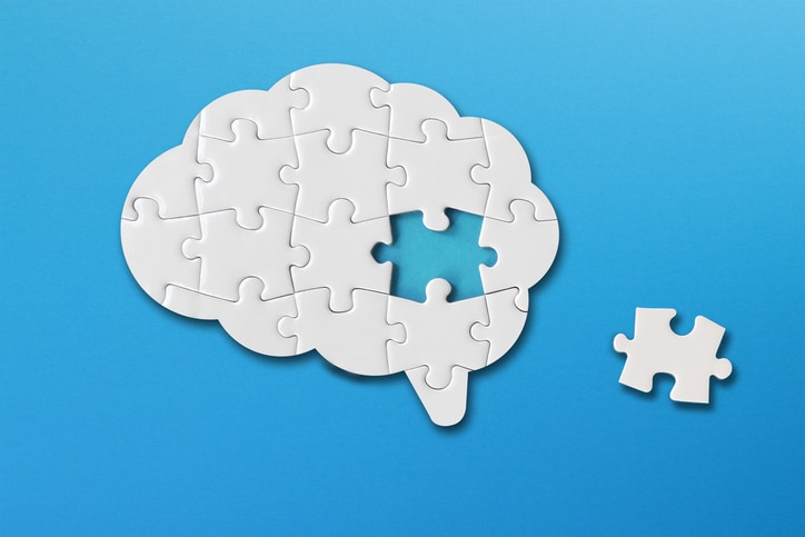 Puzzle pieces forming a brain shape with one piece missing, set against a blue background.
