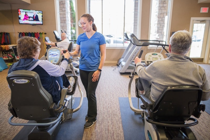 Residents in a senior living community exercise with a fitness trainer on stationary bikes.
