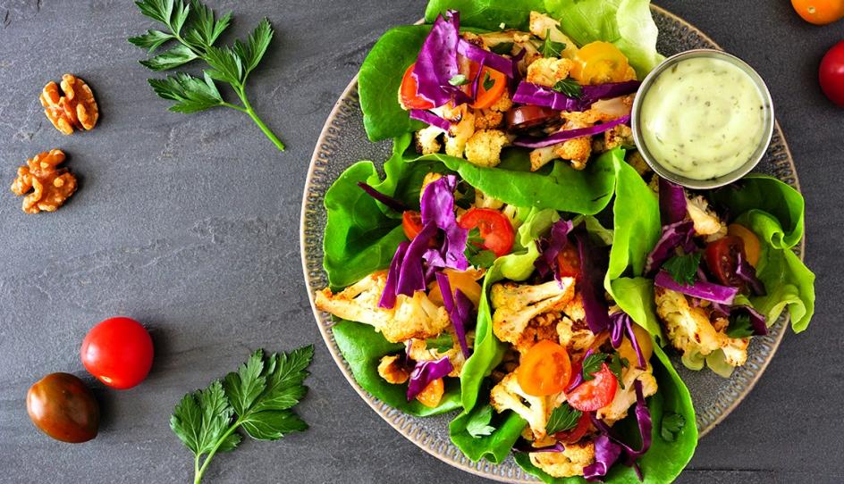 A plate of colorful cauliflower lettuce wraps with tomatoes, red cabbage, and a side sauce.