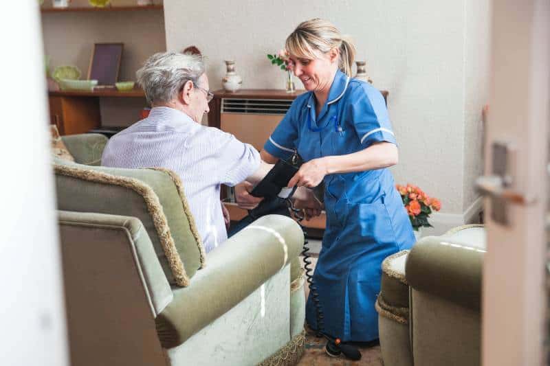 Caregiver assisting senior man in living room of a unit at an assisted living community.