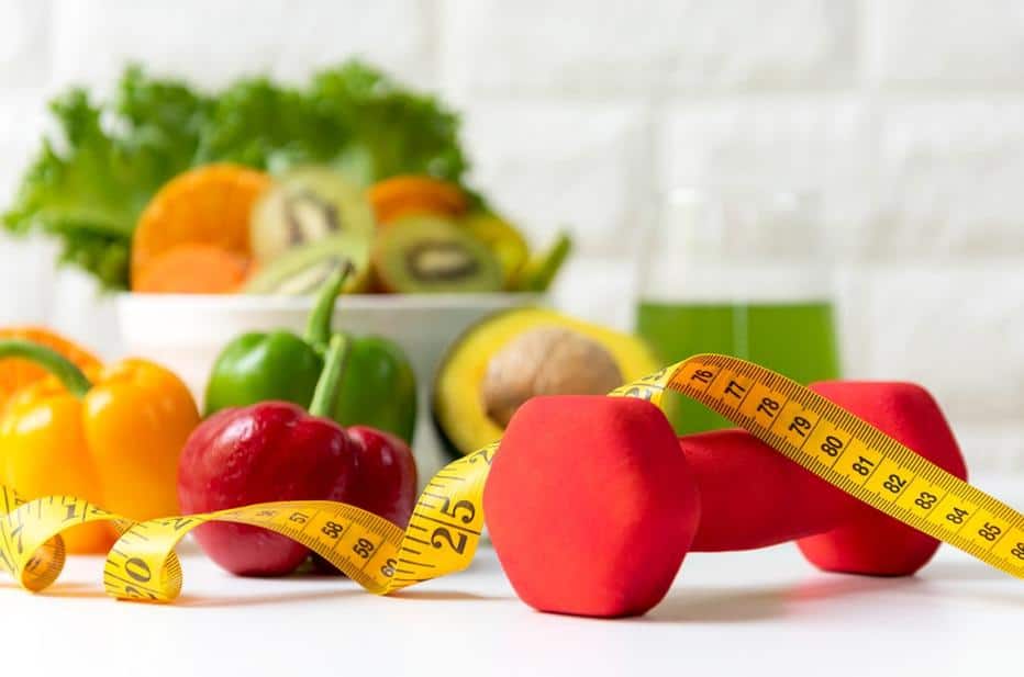 Colorful vegetables, fruits, dumbbells, and a measuring tape for a healthy lifestyle.