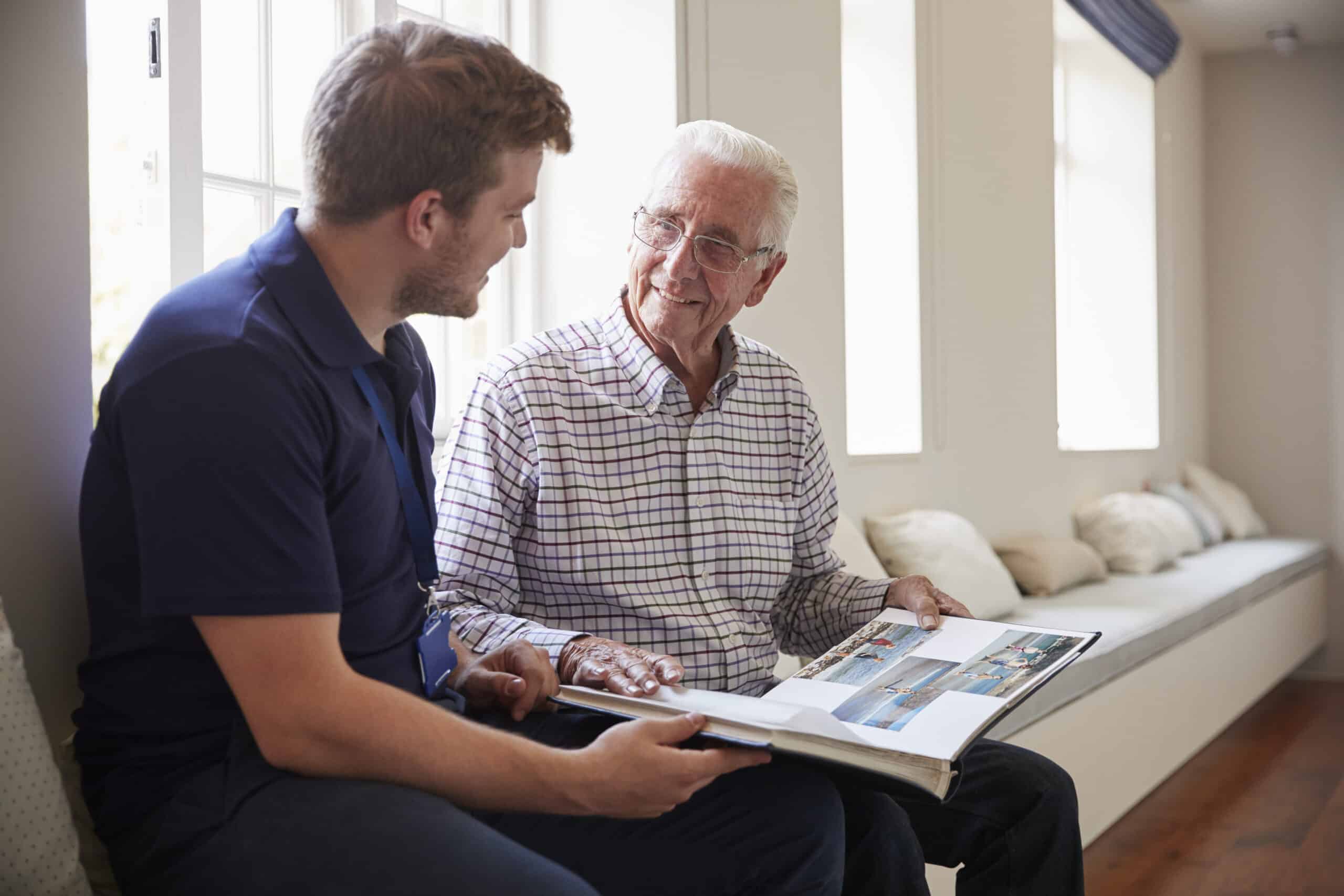 Elderly man sharing a photo album with a young man in a sunlit room.