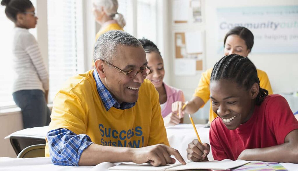 Smiling man helping a child with homework at a community center table.