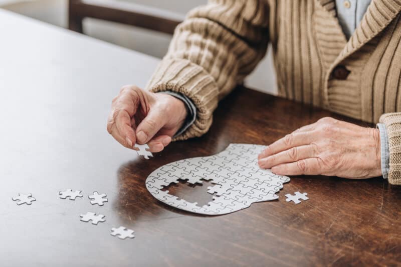 Senior individual assembling a brain-shaped jigsaw puzzle on a wooden table.
