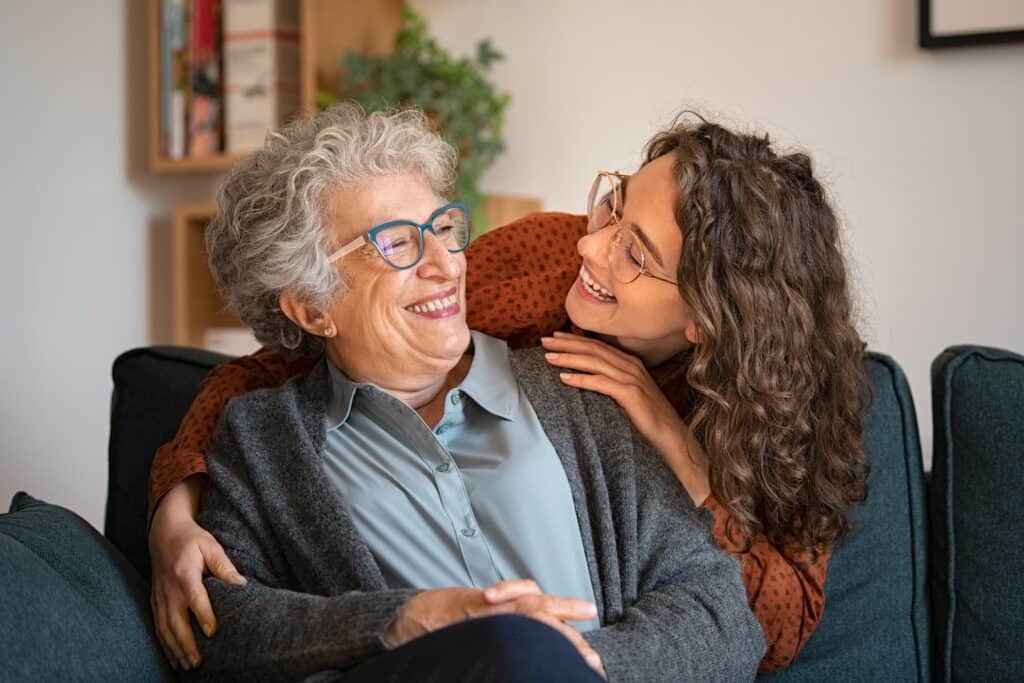 young caregiver embraces and smiles at senior woman