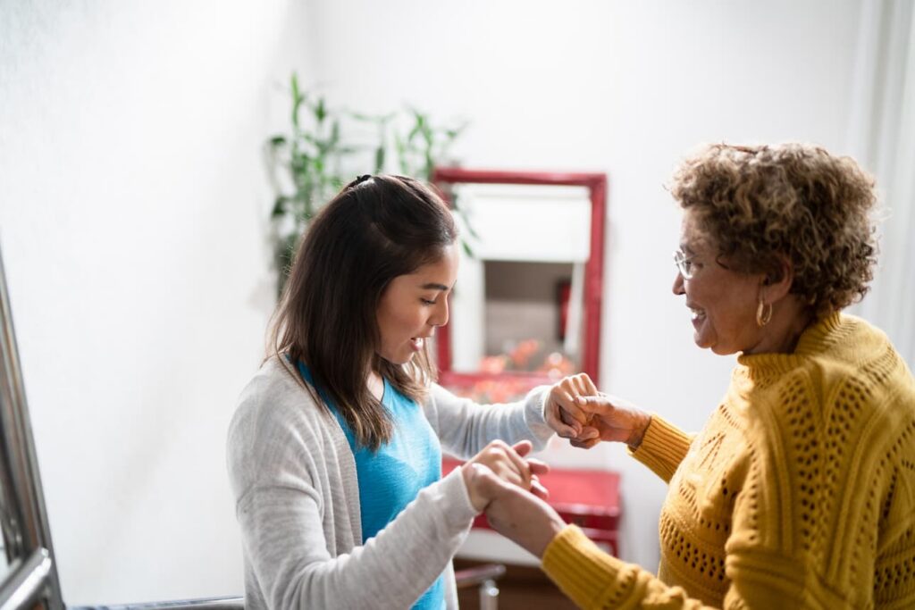Young woman holds senior woman's hands as she helps her from falling
